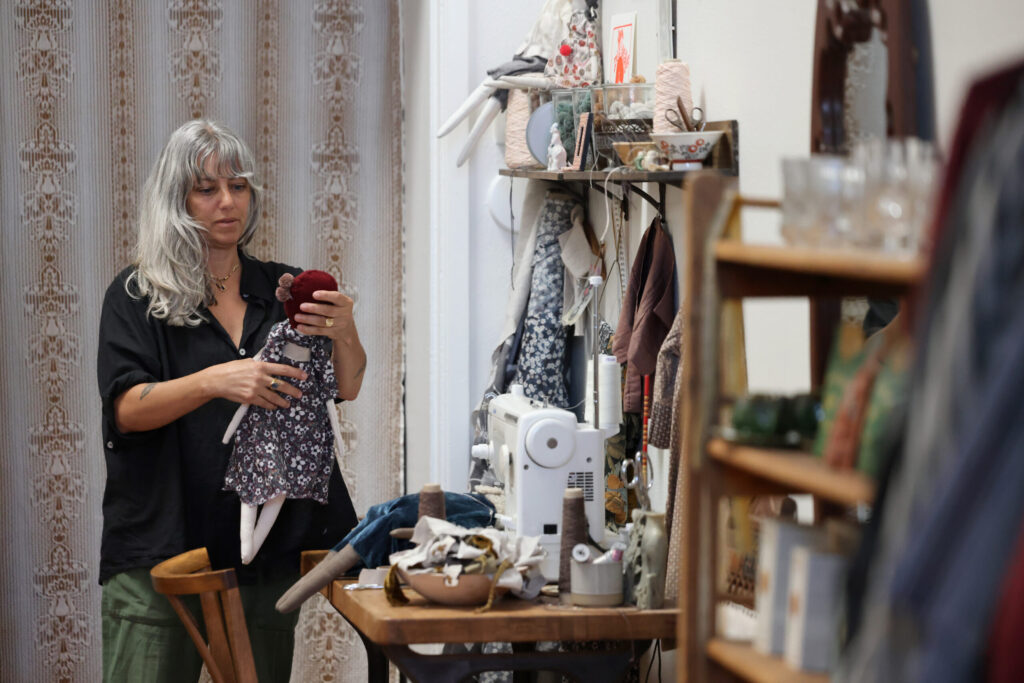 Jess Brown dresses one of her artisan rag dolls for sale at Jess Brown Designs in Petaluma Thursday, Sept. 18, 2025. (Beth Schlanker / The Press Democrat)