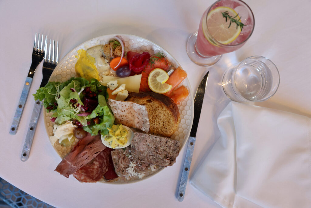 A plate featuring beet cured gravlax, cold and hot smoked salmon, assorted cheeses, charcuterie, elk pate, pig head terrine, a deviled egg, mixed greens, and Nordic breads, served with the Svea Spritz mocktail during a holiday julbord at Stockhome in Petaluma Sunday, Dec. 14, 2025. (Beth Schlanker / The Press Democrat)