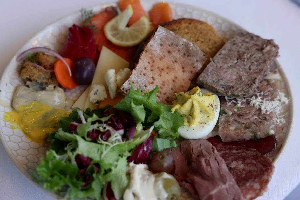 A plate featuring beet cured gravlax, cold and hot smoked salmon, assorted cheeses, charcuterie, elk pate, pig head terrine, a deviled egg, mixed greens, and Nordic breads during a holiday julbord at Stockhome in Petaluma Sunday, Dec. 14, 2025. (Beth Schlanker / The Press Democrat)