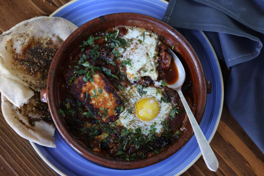 Shakshuka stew with chickpeas, peppers and tomatoes, with griddled halloumi cheese, baked eggs and a side of pita at Pearl Petaluma in Petaluma Thursday, Jan. 8, 2026. (Beth Schlanker / The Press-Democrat)