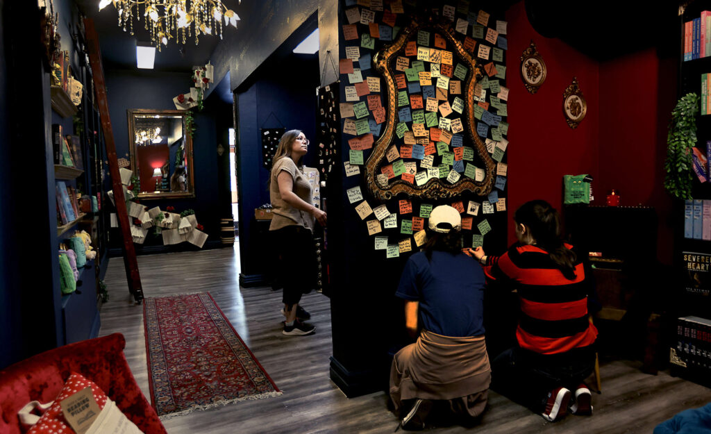 Sisters Amelia and Annabella Cosci write words of appreciation on a sticky note wall at the Velvet Chapter Bookstore in Petaluma, Tuesday, August 19, 2025. At left is their mother Jessica Cosci. (Kent Porter / The Press Democrat)