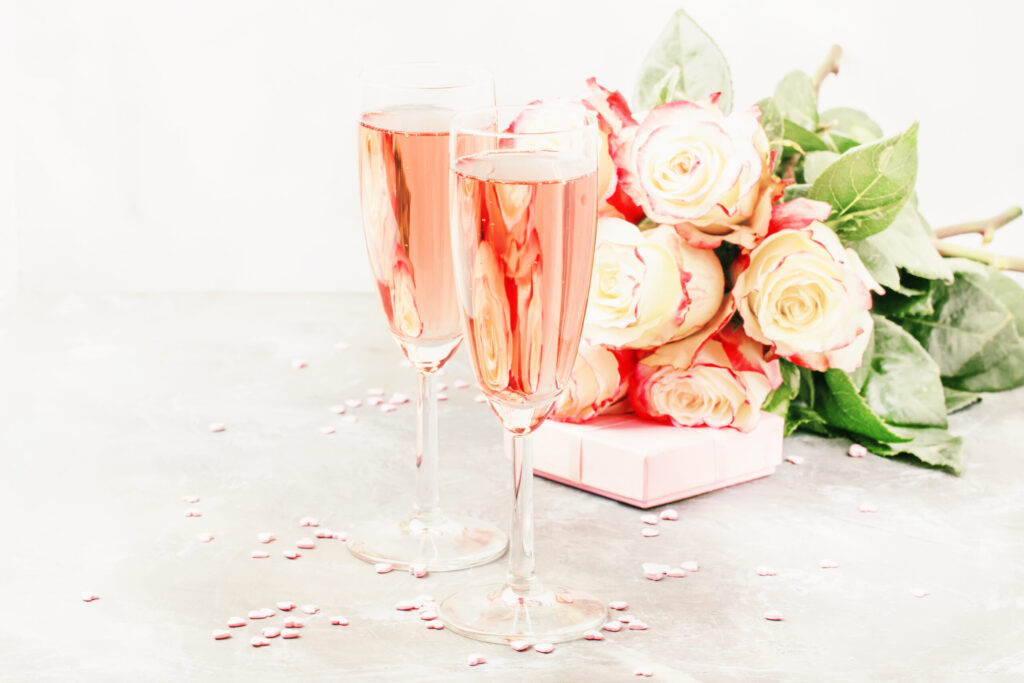 Bouquet of white and red roses, gift box, glasses with pink or rose champagne or sparkling wine for pair for St. Valentines Day, wedding, gray background, selective focus