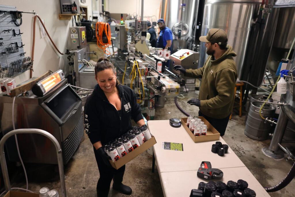 Katie Kirby, left, and Gabriel Gutierrez, right, receive cans as they come off the canning line at Sonoma Springs Brewing Co. in Sonoma Tuesday, Feb. 3, 2026. (Beth Schlanker / The Press-Democrat)