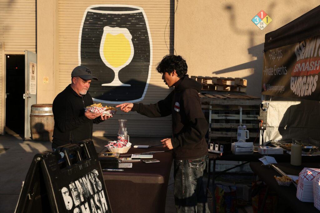 Jayden Flores, of Benny’s Smash Burgers, hands George Lincoln his food order at Cooperage Brewing Company in Santa Rosa on Tuesday, February 3, 2026. (Christopher Chung/The Press Democrat)