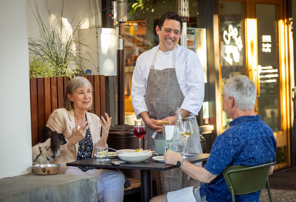 Juju’s chef Jason Pringle chats with locals Shirlene, left, and Robin Bastar on the patio of Acorn Café, transformed into a French-Moroccan dinner pop-up Thursday through Sunday on the square in Healdsburg. Photo taken Thursday, March 19, 2026. (John Burgess/The Press Democrat)
