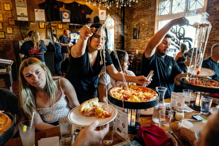 Servers and customers reach to the sky trying to separate slices of gooey, stringy deep-dish pizzas for a family birthday at Old Chicago Pizza Thursday, March 19, 2026 in Petaluma. (John Burgess/The Press Democrat)