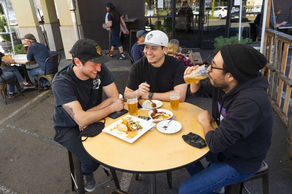 From left, Nick Gonzalez, Julian Romero and Ramo Alviso grab some food and a beer at the Fogbelt Brewing Co. in Santa Rosa on Friday, March 12, 2021. New state laws will allow breweries to serve beer without food beginning Saturday. Fogbelt, because it operates as a restaurant under pandemic rules, will continue to have to serve a meal with its beers, but will be able to allow indoor dining once Sonoma County moves into the less restrictive red tier. (Photo by John Burgess/The Press Democrat)