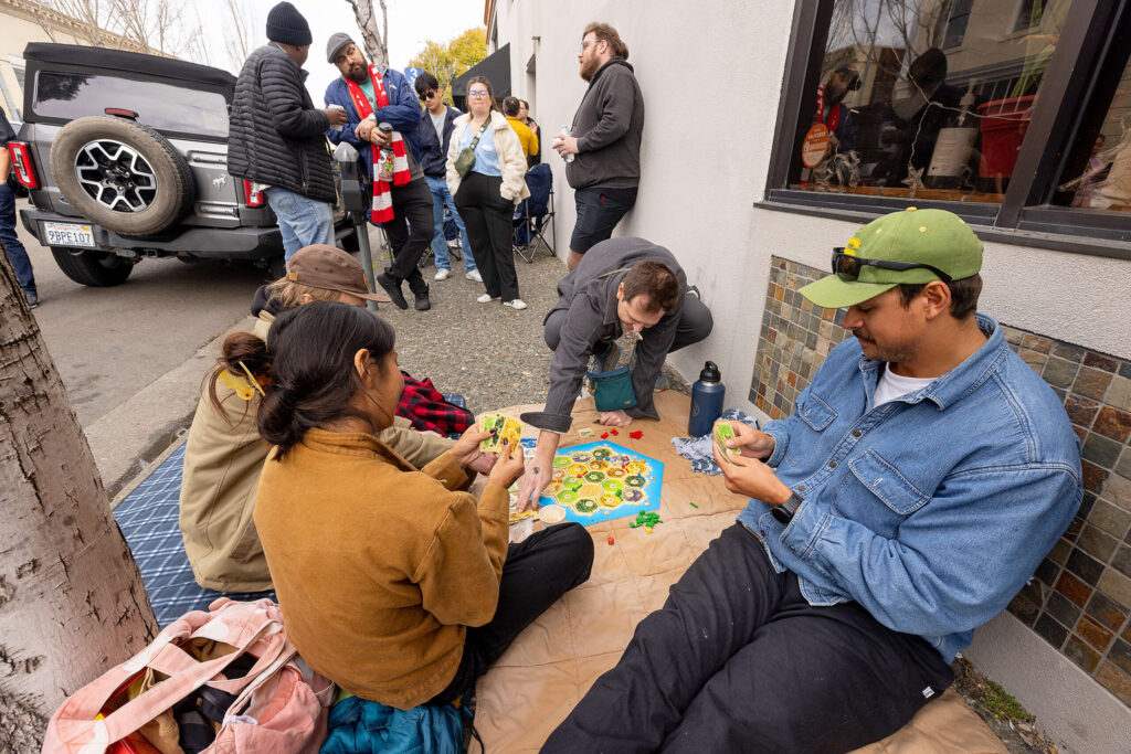 Friends play a board game while waiting in line Friday morning March 21, 2025 for the release of Pliny the Younger triple IPA from the Russian River Brewing Co. in downtown Santa Rosa. (John Burgess / The Press Democrat)