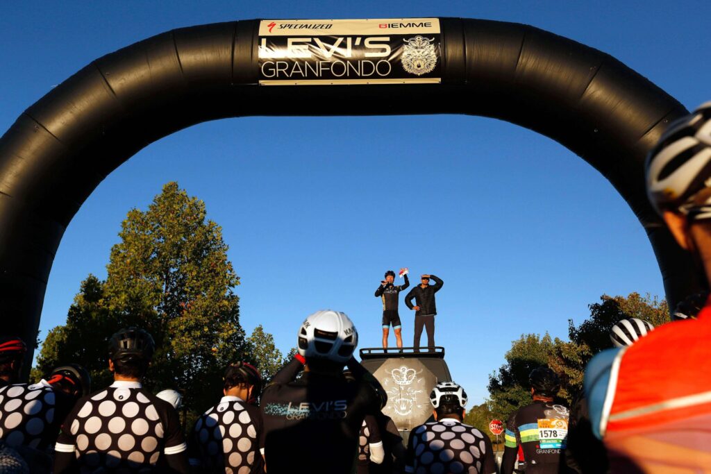Levi Leipheimer and Bike Monkey founder Carlos Perez stand atop Levi's sprinter van to welcome thousands of cyclists riding in the 10th Levi's GranFondo at A Place to Play in Santa Rosa on Saturday, October 6, 2018. (Alvin Jornada / The Press Democrat)