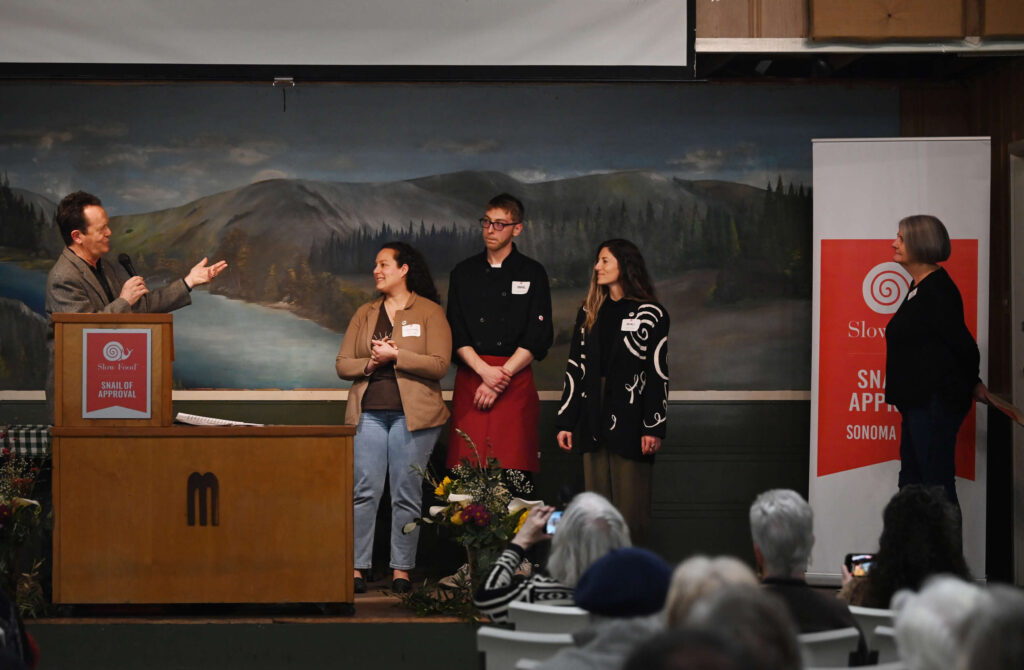 Award winners, Samantha Ramey, Daniel Heitmeyer and Anjuli Lucas of Americana with host Brad Whitworth, far left, and award presenter Carol Diaz, far right, during the Snail of Approval awards ceremony held at Grange Hall in Sebastopol, Wednesday, Feb. 28, 2024. (Erik Castro / For The Press Democrat)