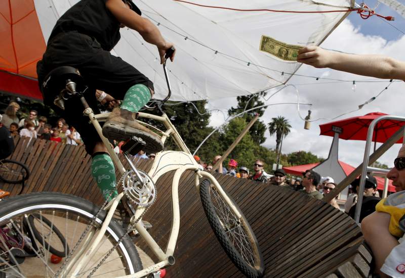 A child holds out a dollar for Josh Thwaites as he rides his bike in the Whiskeydome, a wooden velodrome, built by Whiskey Drunk Cycles during the Great Handcar Regatta in Santa Rosa, on Sunday, September 25, 2011. (Beth Schlanker/ The Press Democrat)