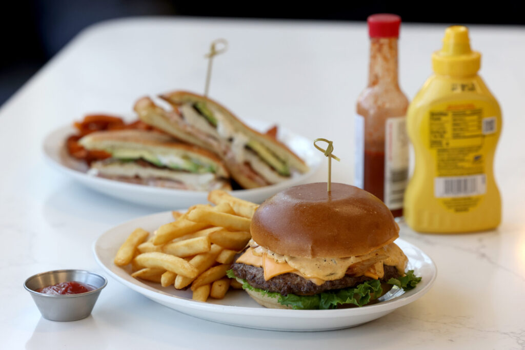 The Classic burger with American cheese, onion, pickles lettuce, and house-made Pressed sauce, with a side of fries, and the Chicken Ranch sandwich, rear, at Pressed in Rohnert Park Friday, April 17, 2026. (Beth Schlanker / The Press Democrat)