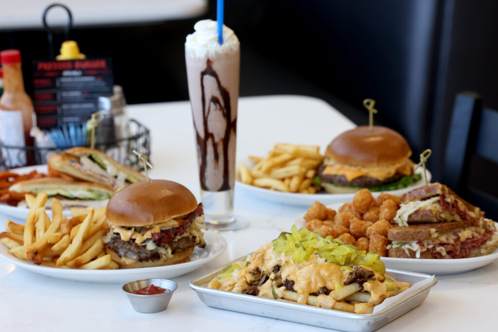 (Clockwise from bottom) The Classic loaded fries, P & B burger with fries, the Chicken Ranch, a chocolate milkshake, the Classic burger with fries, and the Reuben sandwich with tater tots at Pressed in Rohnert Park Friday, April 17, 2026. (Beth Schlanker / The Press Democrat)