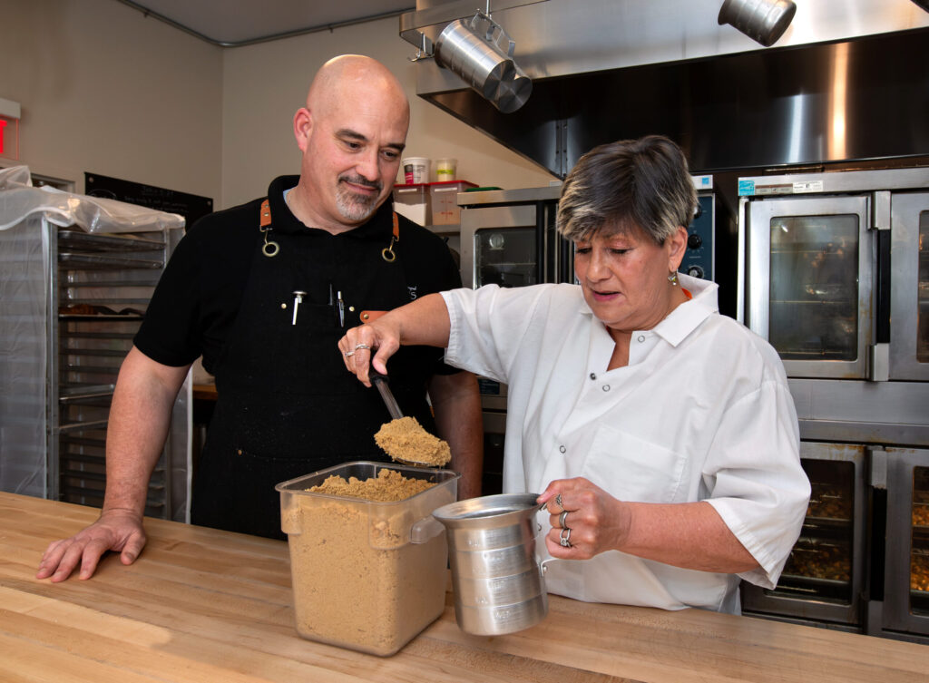 Paul Haddorff, director of food services for Redwood Gospel Mission, helps student, Allison Spears of Santa Rosa, as she spoons sugar for a muffin mix, at the new Redwood Gospel Baking Company cafe in Santa Rosa, Friday, April 10, 2026. (Darryl Bush/For The Press Democrat)