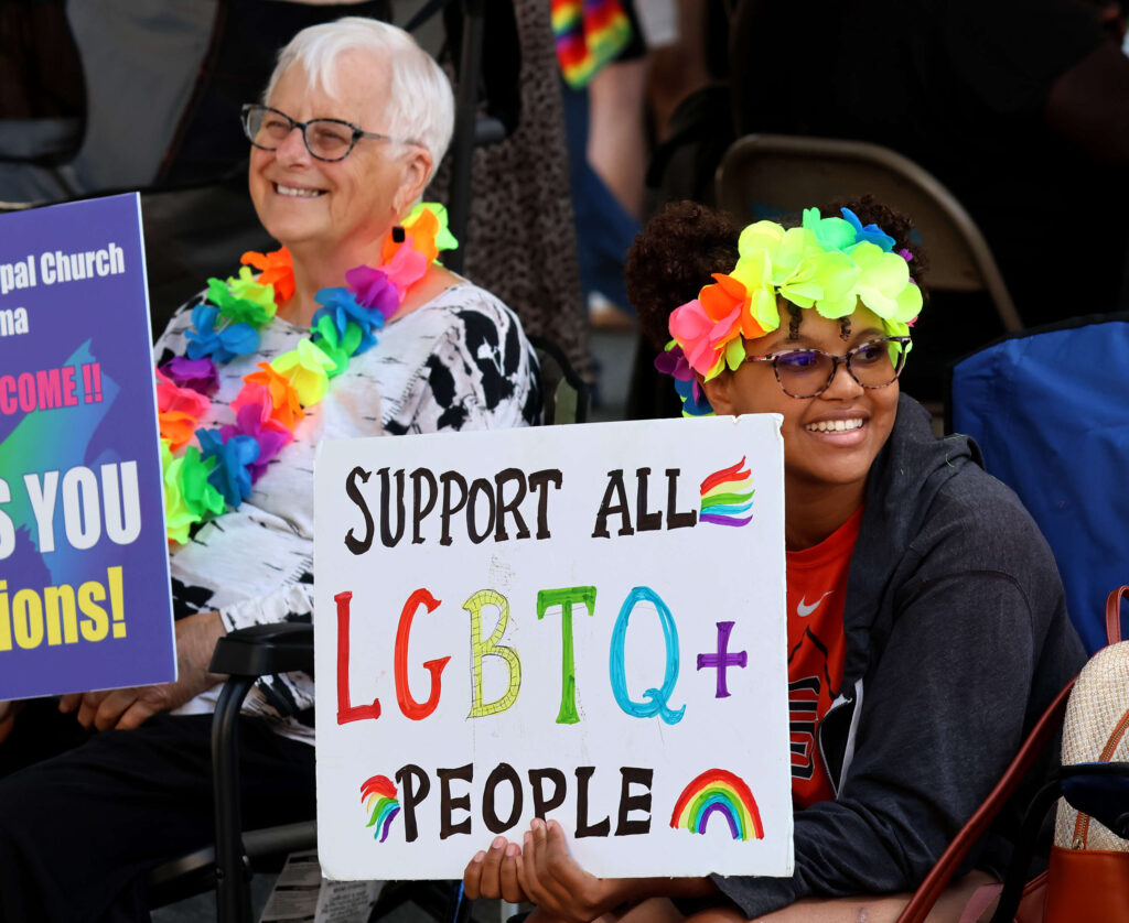 Kasandra Williams, 15, of Santa Rosa, holds a sign with Geri Olson of Petaluma, back left, as they wait for the 2025 Sonoma County Pride Parade in Santa Rosa on Saturday, May 31, 2025. (Darryl Bush / For The Press Democrat)