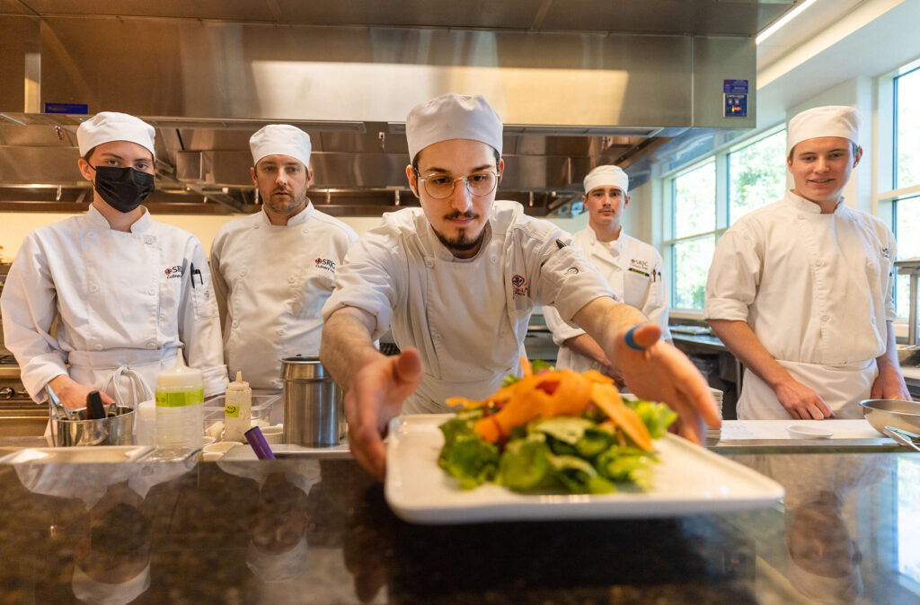 Brandon Nickel carefully places the first dish for lunch service Thursday, April 20, while other Santa Rosa Junior College culinary students look on at Café Rose, a campus restaurant that opened for regular service Thursday for the first time since the start of the pandemic. (John Burgess / The Press Democrat)