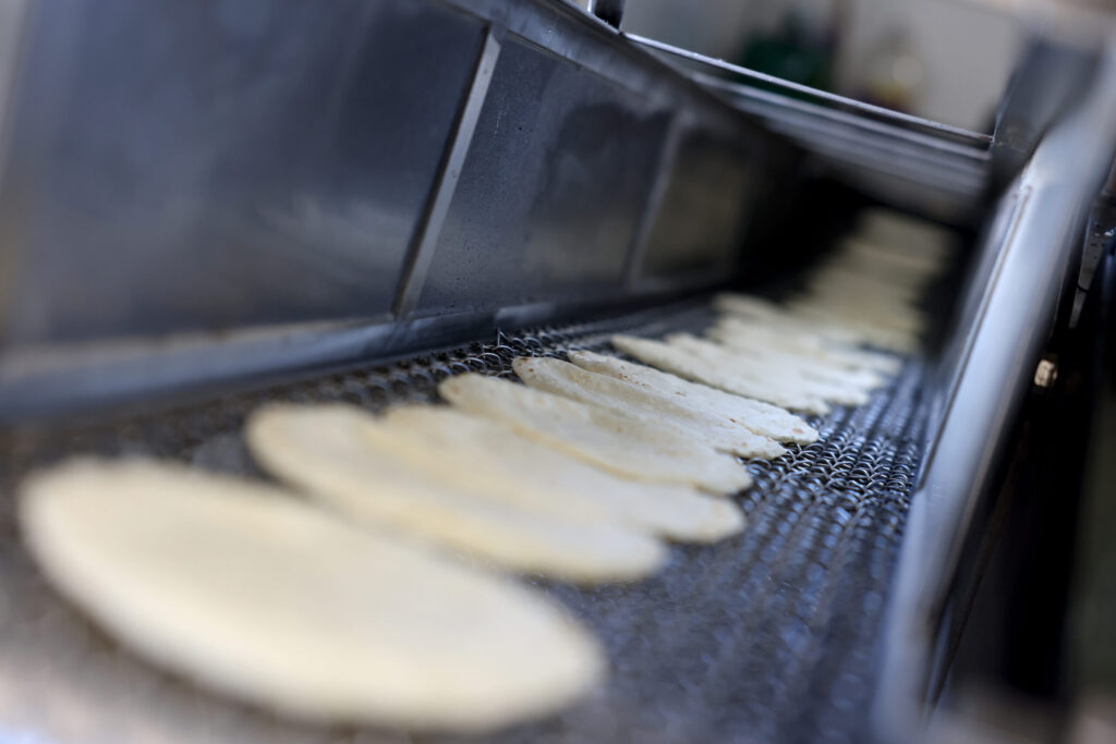 Freshly pressed tortillas run along a conveyor belt at Tortilleria Apatzingan in Santa Rosa Tuesday, July 8, 2025. (Beth Schlanker / The Press Democrat)