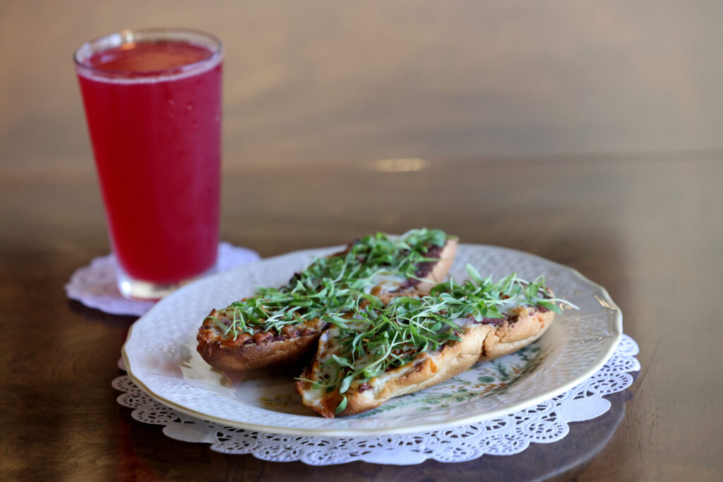 Molletes, El Salvadoran red beans and melted Oaxaca cheese on a Mexican bread roll and topped with microgreens, with a pint of Cooperage’s Fruit Punch Sparklepants at Sandpino’s Coffee and Brews in Rohnert Park Friday, March 27, 2026. (Beth Schlanker / The Press Democrat)