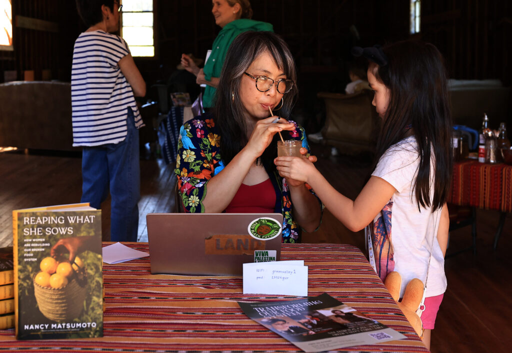 Mai Nguyen samples lemonade prepared by her daughter Minh Nguyen-Nelson during a book signing for author Nancy Matsumoto, background, left, at Green Valley Farm and Mill in west Sonoma County, Sunday, March 22, 2026. (Kent Porter / The Press Democrat)
