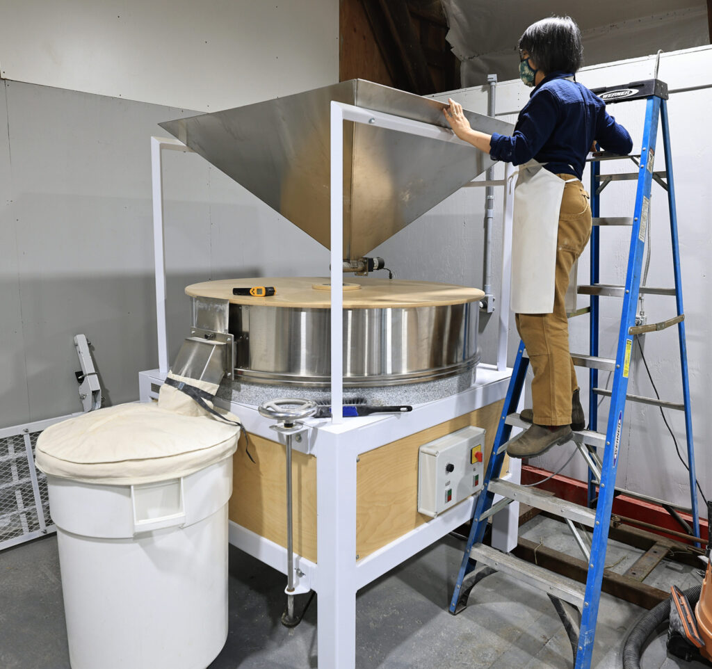 Mai Nguyen begins the process of milling wheat into hard white wheat flour, at Green Valley Farm and Mill in west Sonoma County, Wednesday, March 4, 2026. (Kent Porter / The Press Democrat)