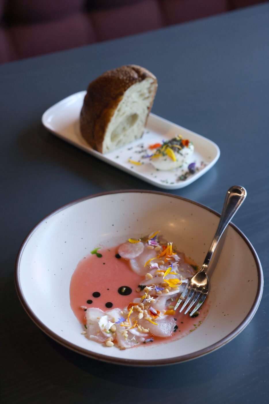 The sliced raw rockfish with strawberry aguachile, radish and pine nuts accompanied by the bread and butter, rear, at Dead Letter restaurant in Sonoma Wednesday, July 15, 2026. (Beth Schlanker / The Press Democrat)