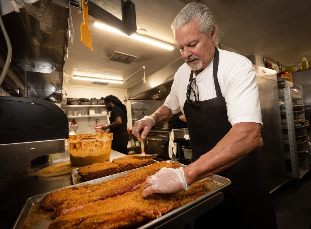 Steven Kobus applies the spice rub to pork and beef ribs in the kitchen at Saucy Mama’s Jook Joint Friday, July 18, 2026 in Guerneville. (John Burgess/The Press Democrat)