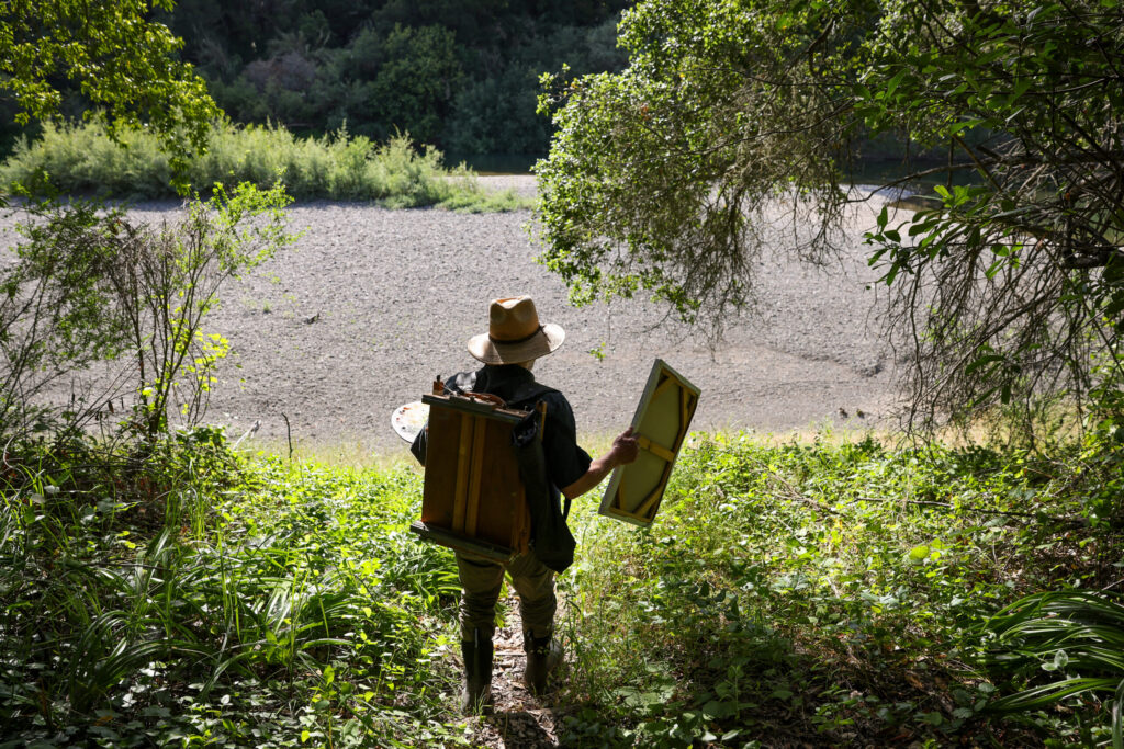 Christopher Leith Evans walks down to the Russian River from his home with his French easel in Healdsburg on Monday, May 11, 2026. (Christopher Chung/The Press Democrat)