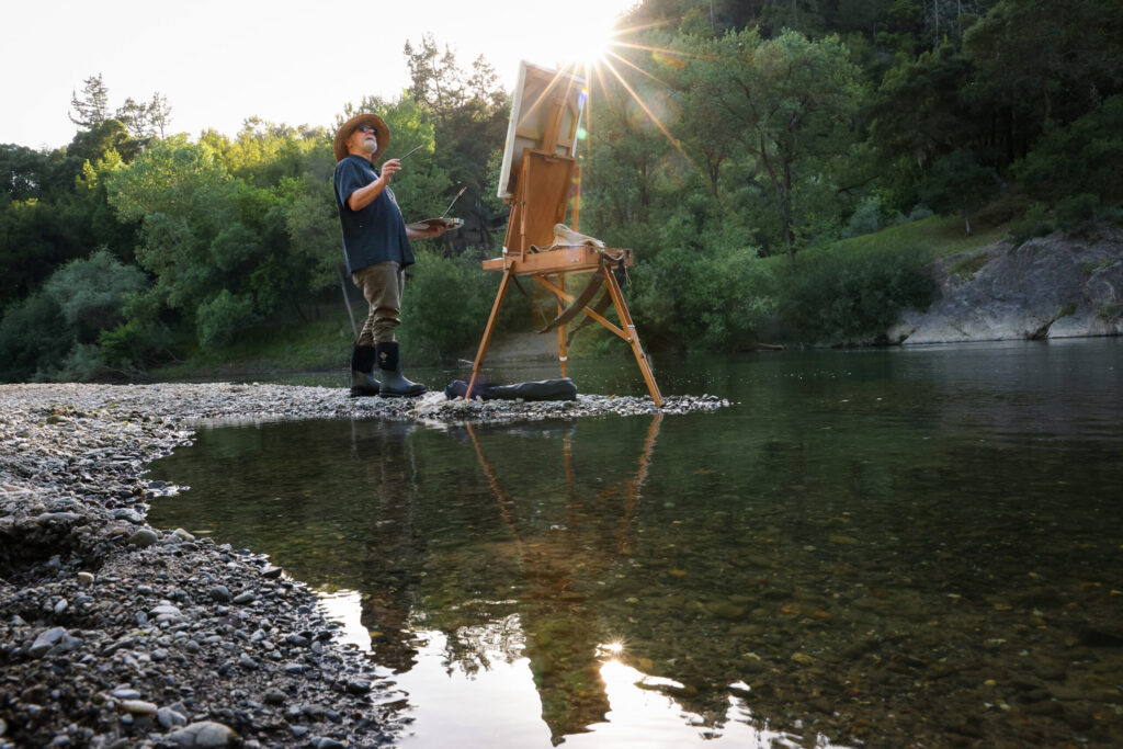 Christopher Leith Evans paints a scene along the Russian River as the sun begins to set near his home in Healdsburg on Monday, May 11, 2026. (Christopher Chung/The Press Democrat)