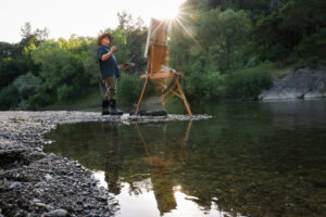 Christopher Leith Evans paints a scene along the Russian River as the sun begins to set near his home in Healdsburg on Monday, May 11, 2026. (Christopher Chung/The Press Democrat)