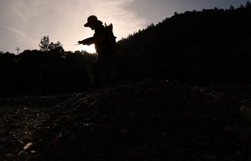 Christopher Leith Evans walks home along the banks of the Russian River with his French easel on his back in Healdsburg on Monday, May 11, 2026. (Christopher Chung/The Press Democrat)