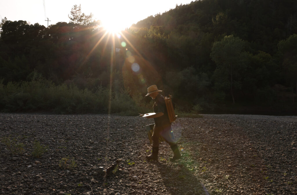 Christopher Leith Evans walks home along the banks of the Russian River with his French easel on his back in Healdsburg on Monday, May 11, 2026. (Christopher Chung/The Press Democrat)