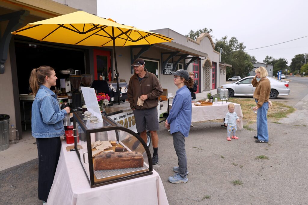 Ferrell Carter, left, talks with customers at the Graton Station in Graton Sunday, Aug. 16, 2026. (Beth Schlanker / The Press Democrat)