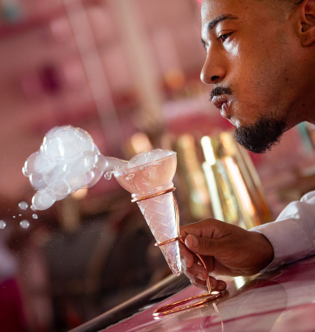 Bartender Johnny On The Rocks encourages guests to make a wish before blowing the smoky top off a High Noon cocktail at Café Carrusel Tuesday, July 28, 2026 in Santa Rosa. (John Burgess/The Press Democrat)